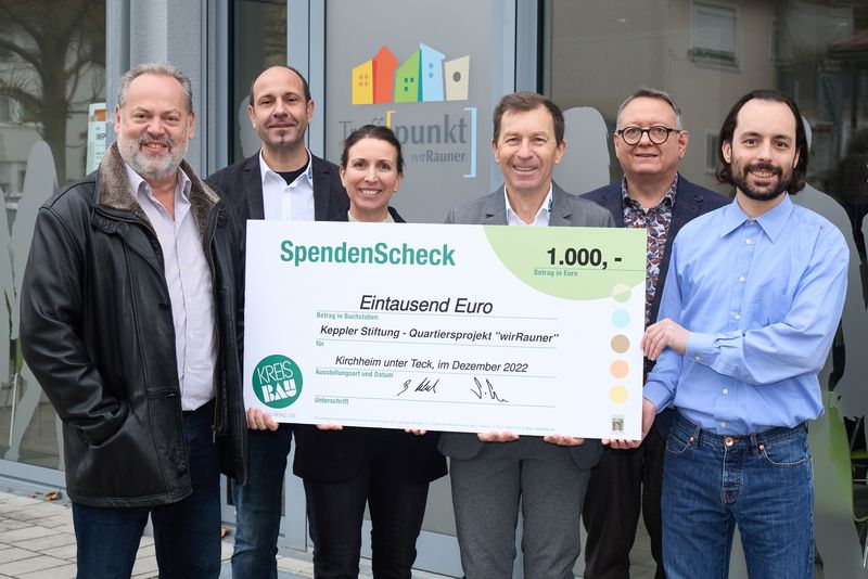 Sechs Personen präsentieren Spendencheck über 1.000 Euro vor Büro