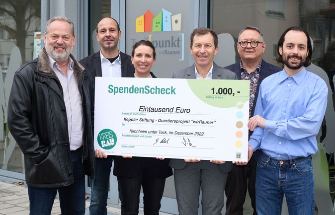 Sechs Personen präsentieren Spendencheck über 1.000 Euro vor Büro